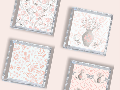 Three square trays with scalloped silver edges featuring pink floral, monogrammed vase, and deer patterns on white.