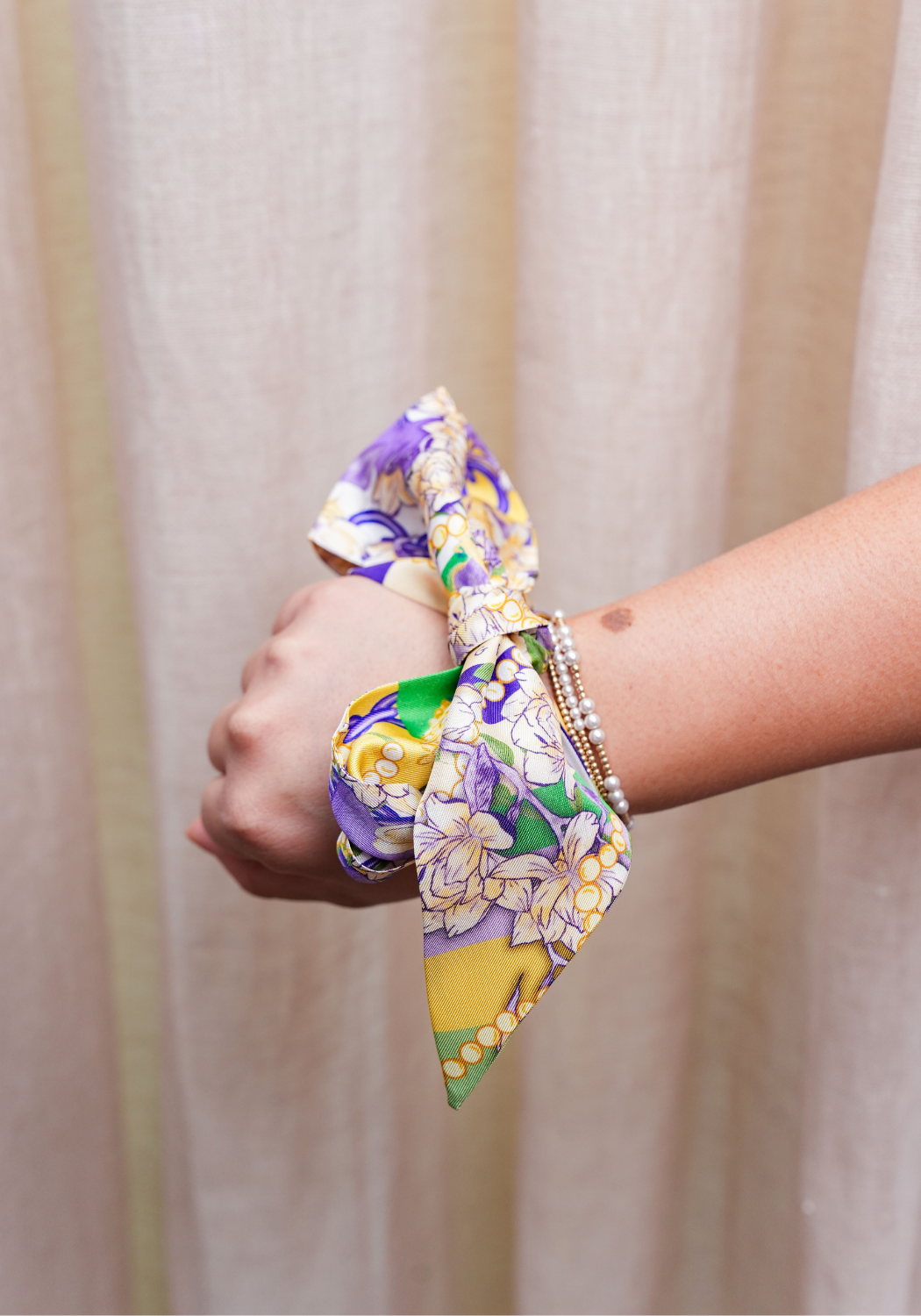 Silk Mardi Party Heirloom Scarflette tied around wrist with purple, yellow, and green floral print.