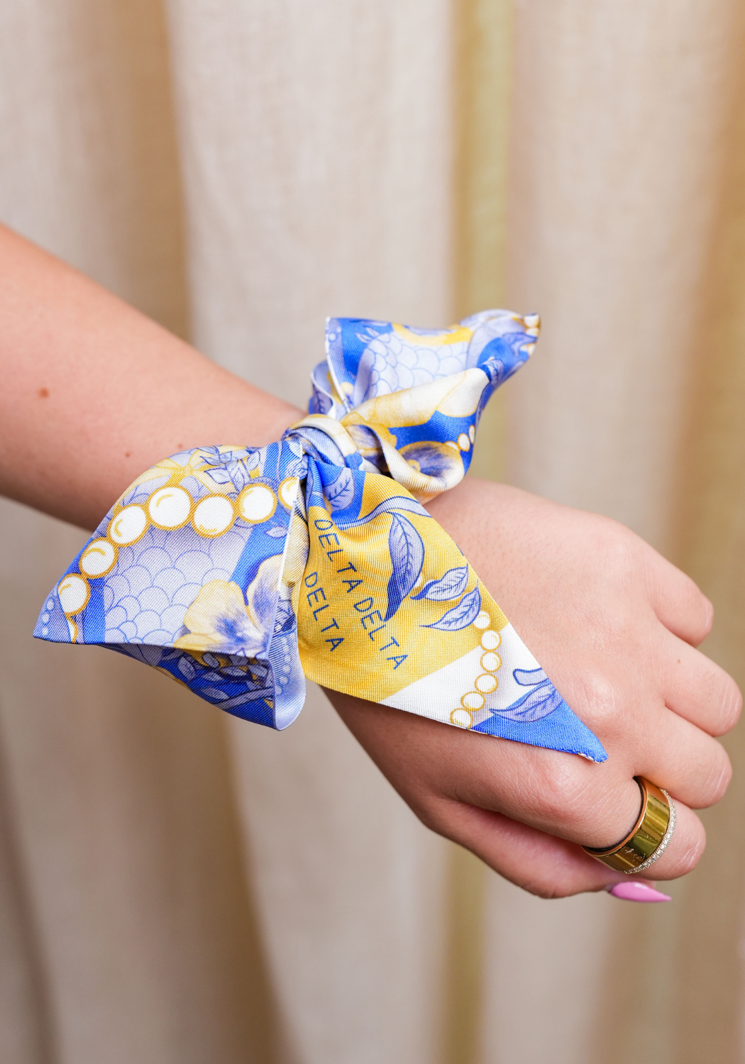Blue and yellow patterned silk scarflette tied around wrist with Delta Delta Delta lettering.