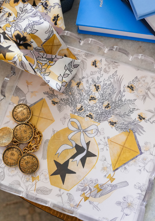 White scalloped tray decorated with gold and black floral and kite illustrations and tied ribbon details.