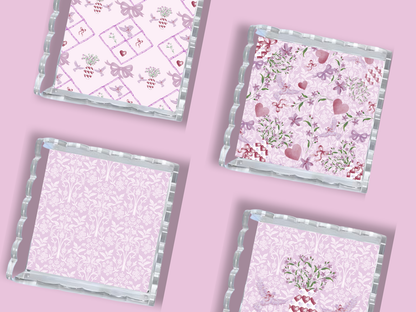 Set of four square trays with scalloped silver edges and pink floral patterns on a lavender background.
