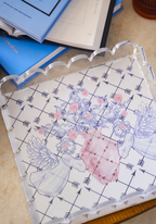 Clear acrylic scalloped tray with floral and winged figures design in pastel colors on patterned base.