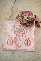 Clear acrylic tray with scalloped edges, pink floral and lyre designs, and a matching floral ribbon looped on top.