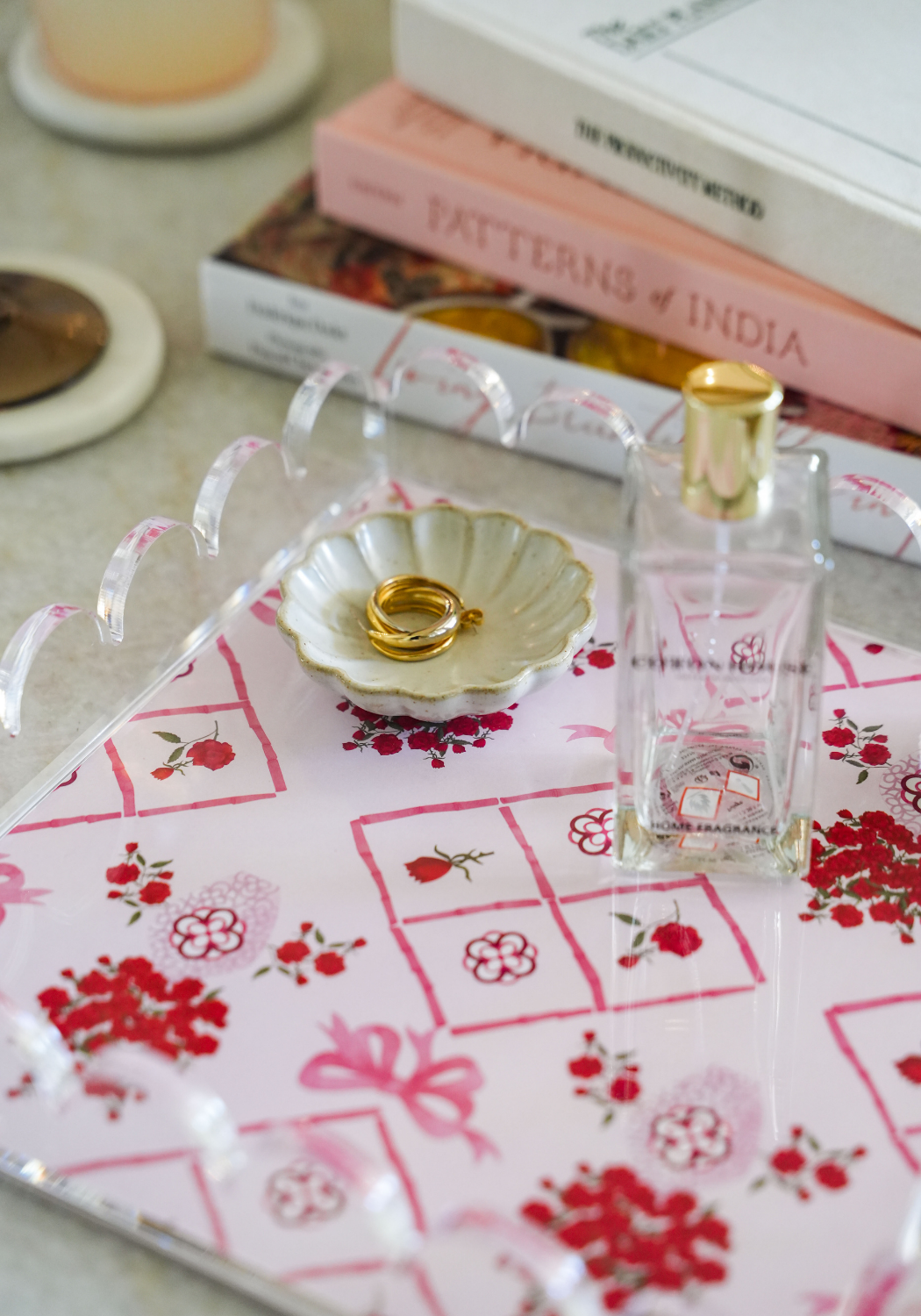 Clear acrylic tray with scalloped edges on pink and red floral fabric, holding a gold shell dish and clear perfume bottle.