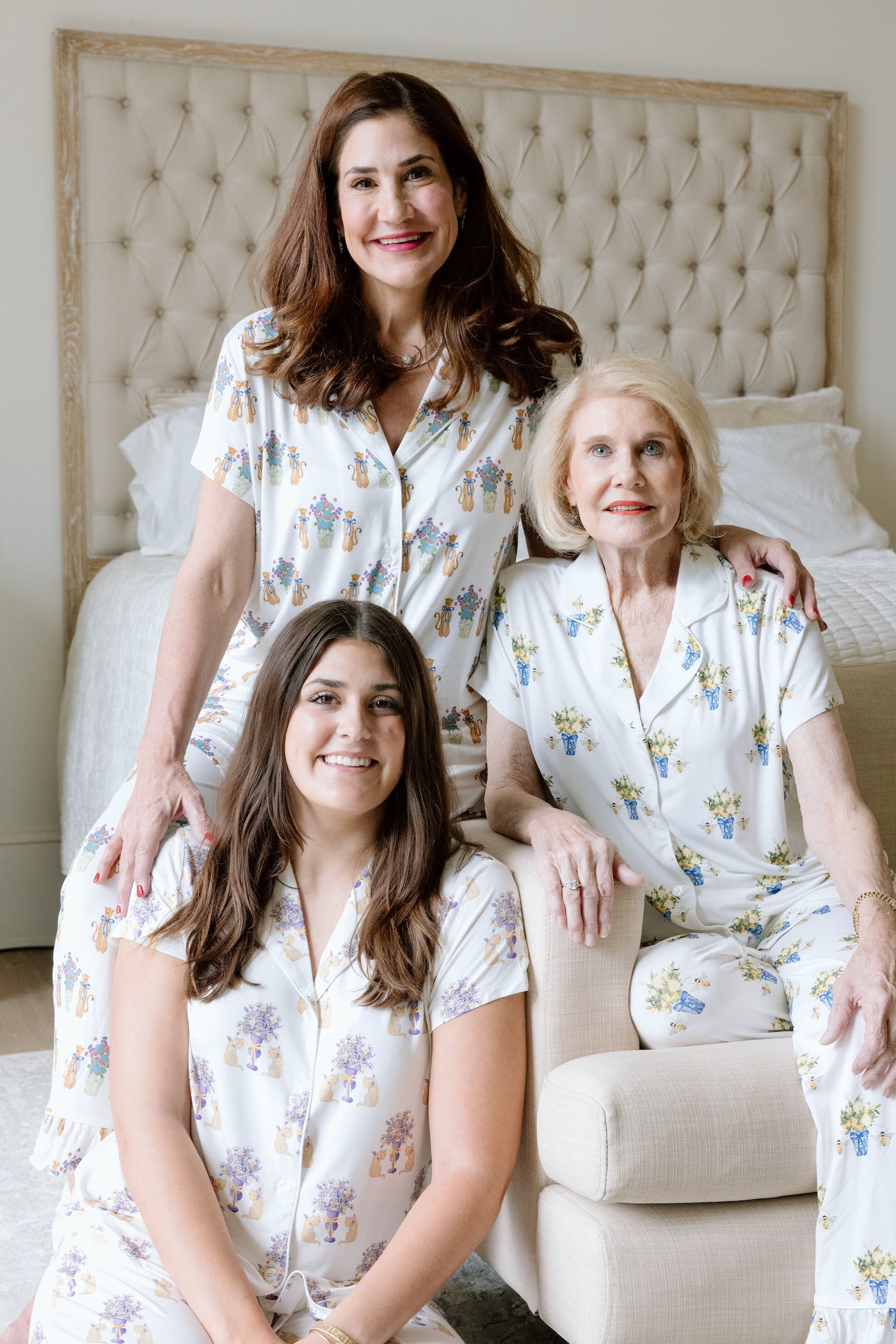 Three women wearing matching white pajama sets with LSU Tigers-themed gold and purple crest prints lounging in a bedroom.