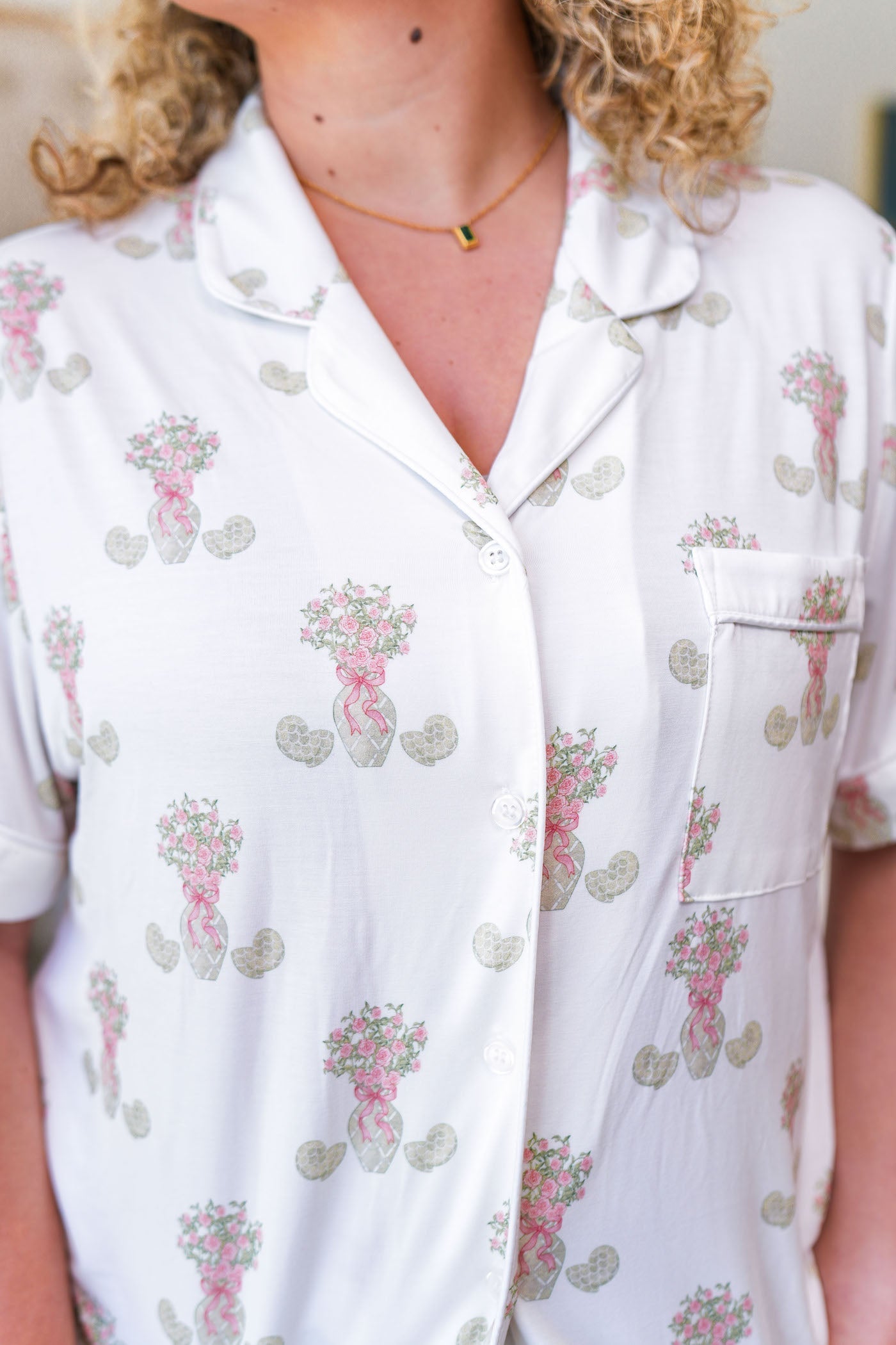 White pajama top with pink floral print, short sleeves, collar, and front pocket with purple trim.
