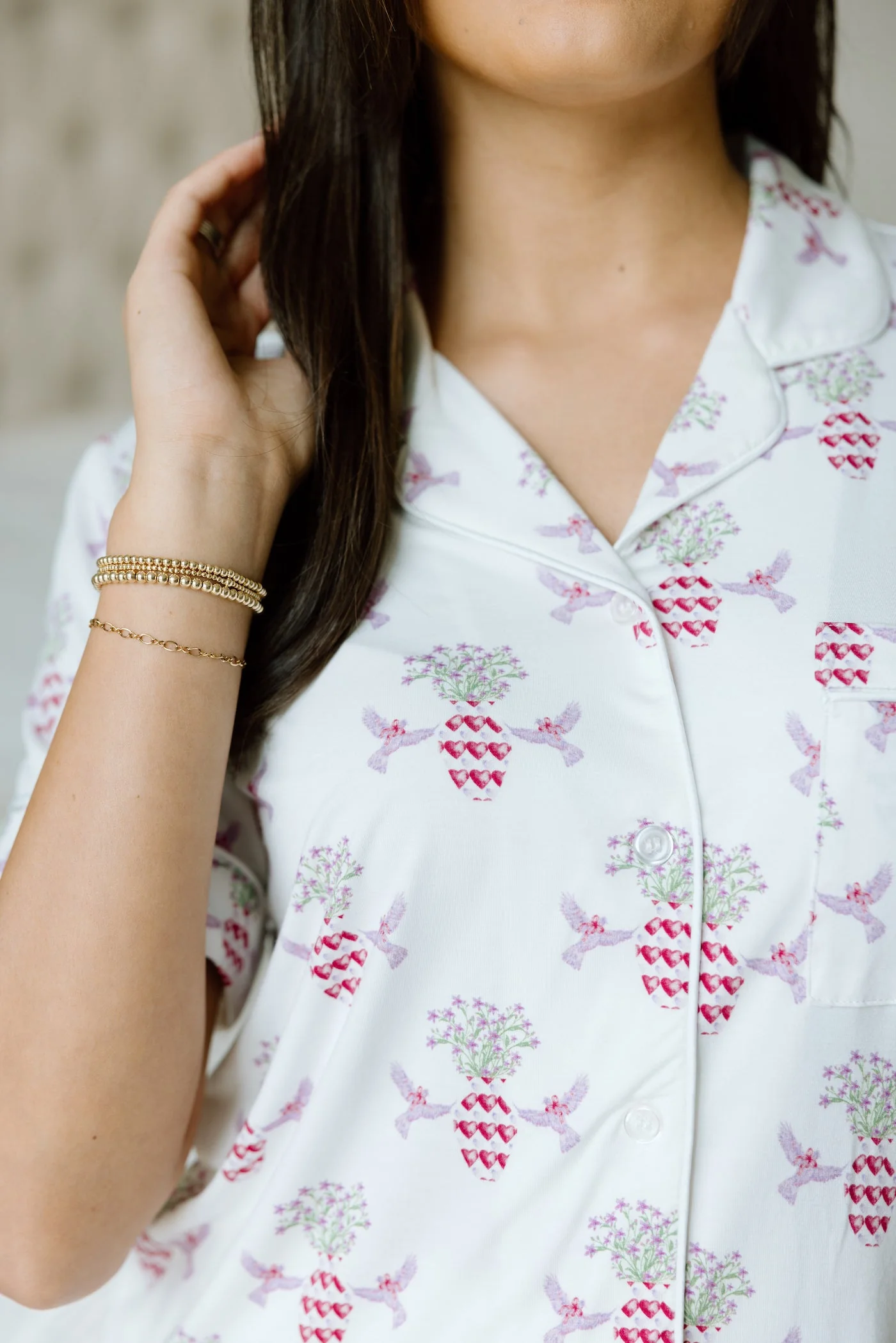 White cotton pajama top with pink pineapple print and black piping, worn by model.