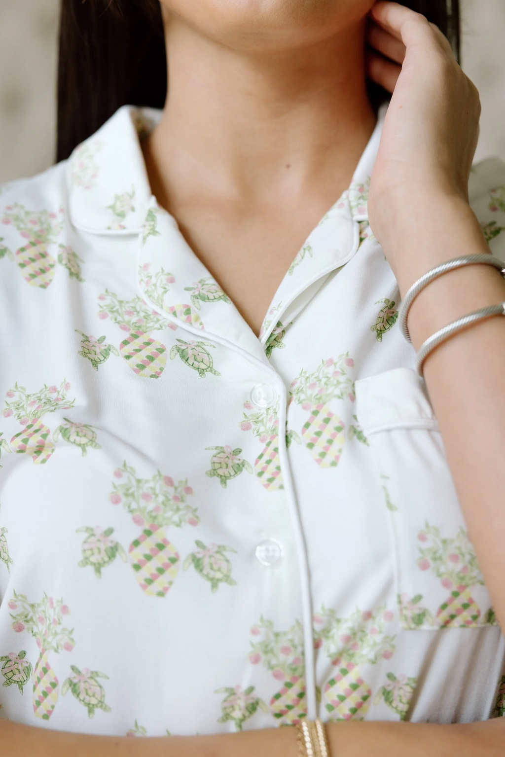 White pajama top with pastel floral and pineapple print, notch collar, and white piping trim.
