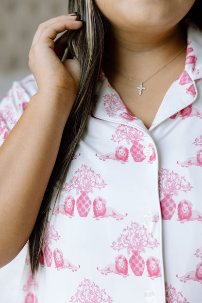White button-up pajama top with pink floral and emblem print, worn with a silver cross necklace.