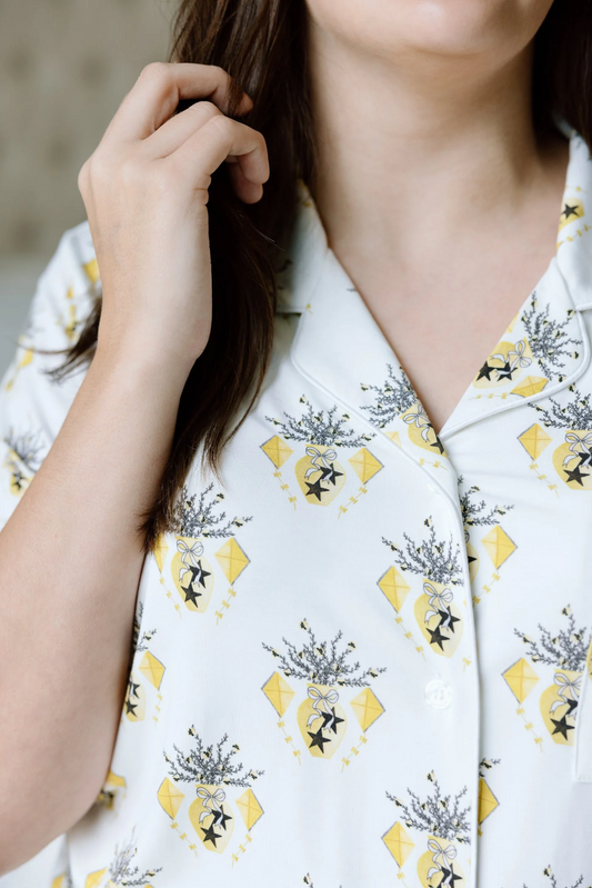 White pajama shirt with yellow diamond and black emblem pattern, notched collar, and buttons.