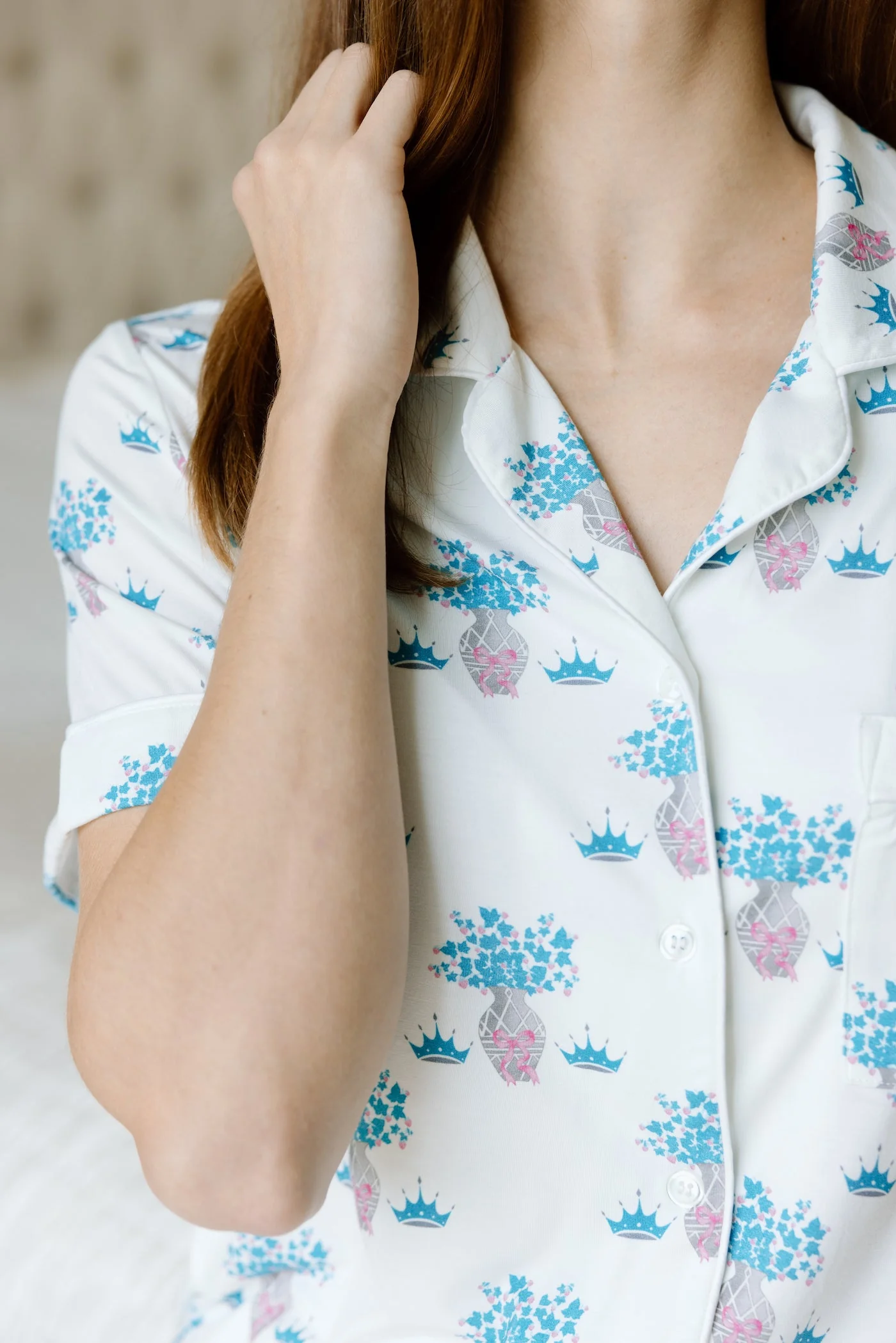 White pajama top with pink crowns and blue floral print, notched collar, and black piping.
