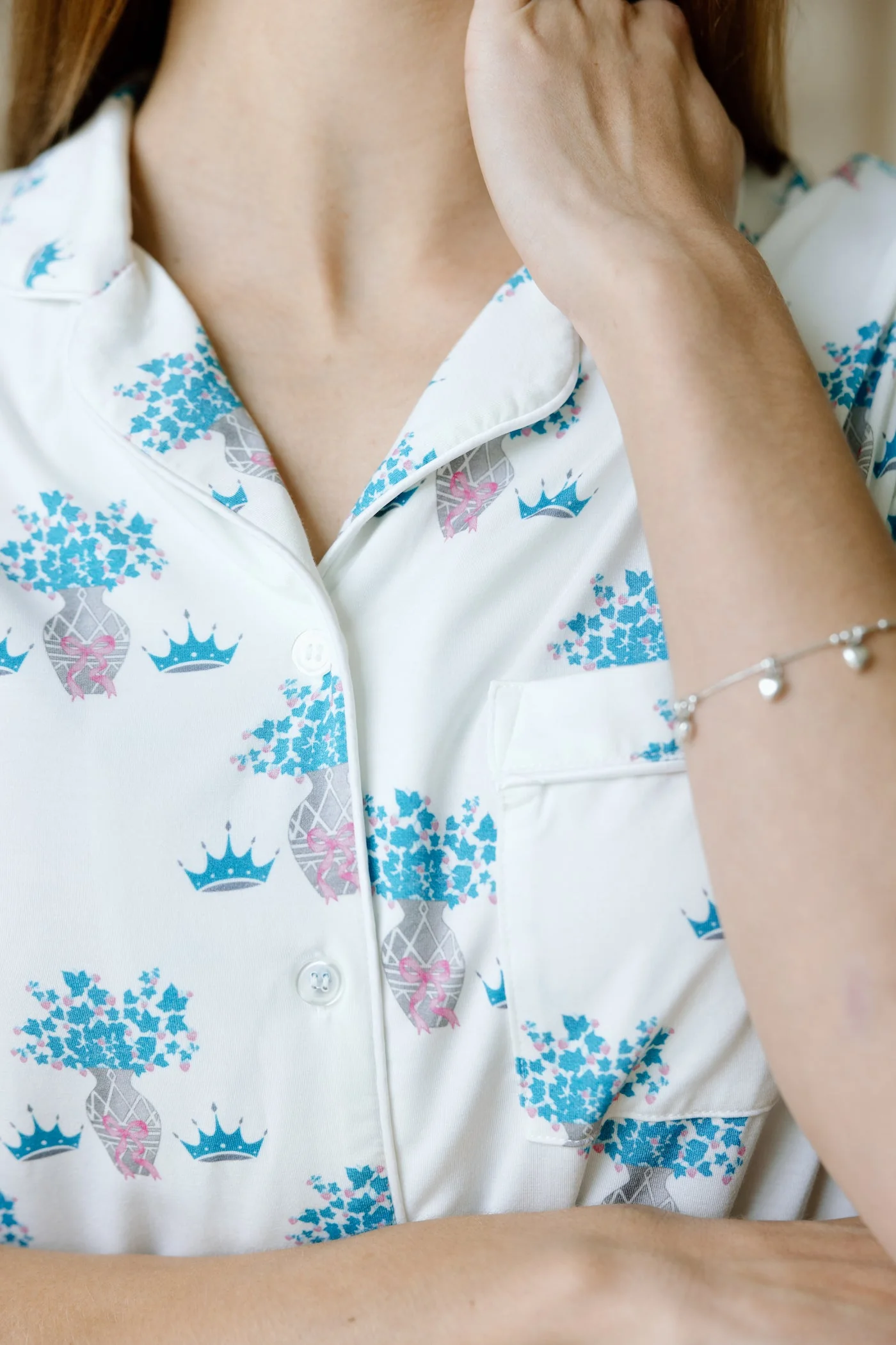 White pajama top with blue and pink floral and crown prints and white piping trim.