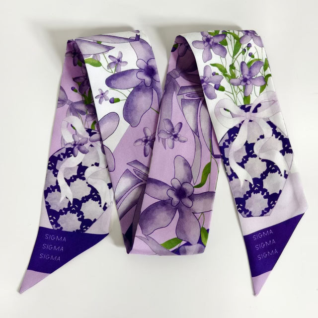 Lavender scarflette with purple floral and geometric patterns, pointed ends with dark purple tips.
